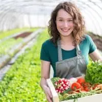 smiling female gardener holding basket with vegetables