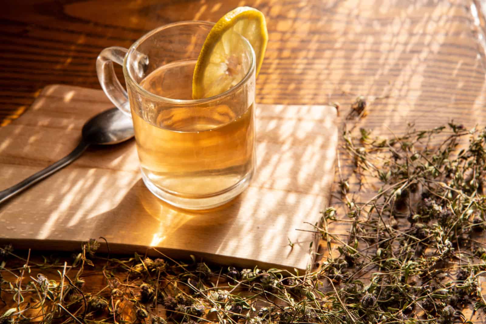 A cup of creeping thyme (thymus serpyllum) tea, with dry creeping thyme twigs on a wooden background