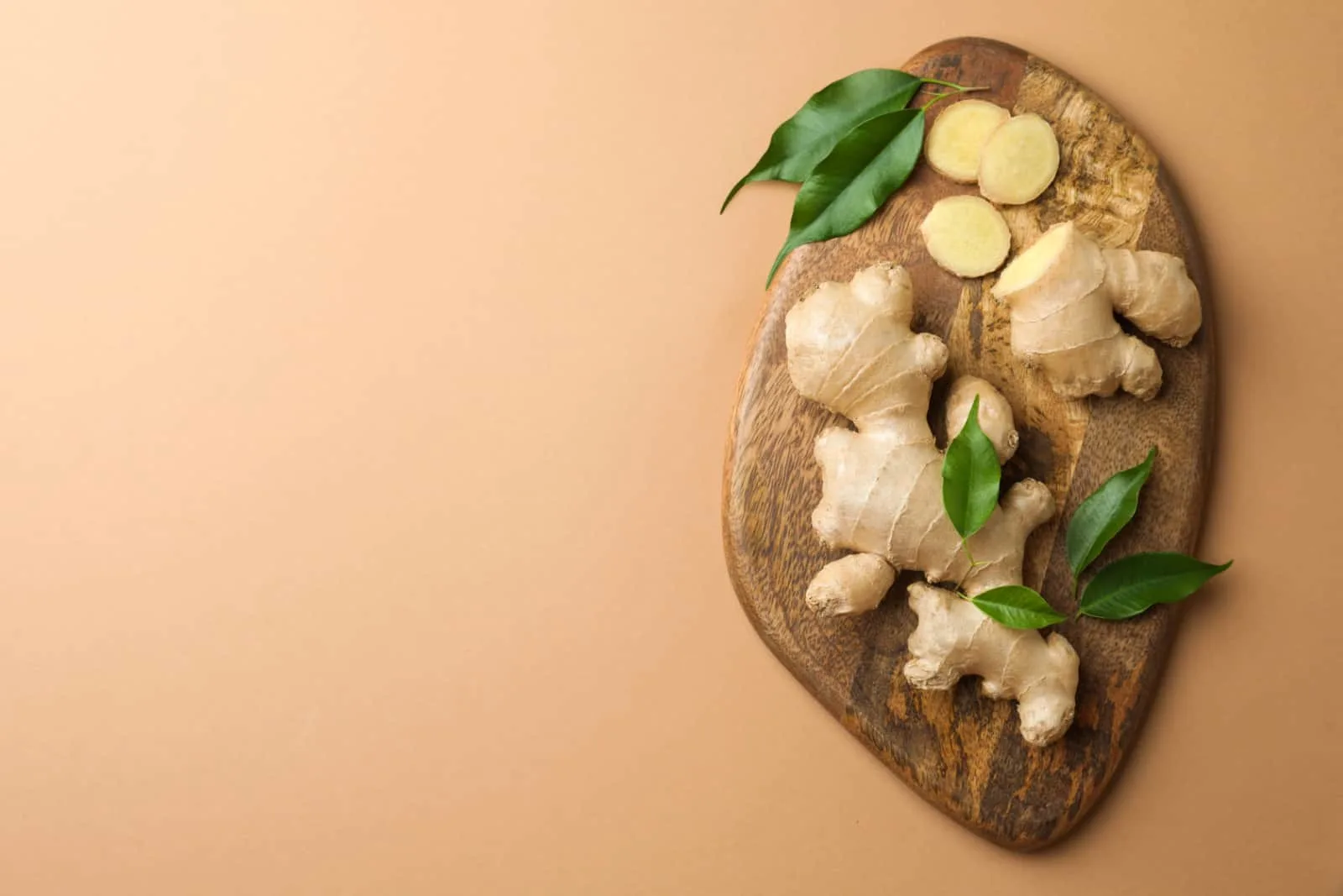 Fresh ginger with green leaves on light pale brown background