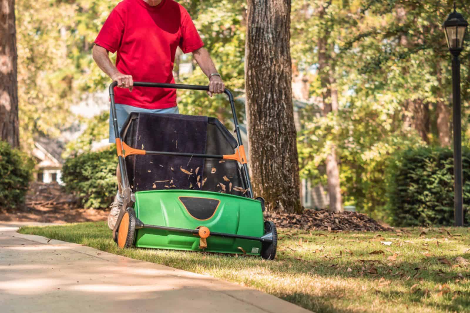 Man using manual push lawn sweeper to remove fall leaves 