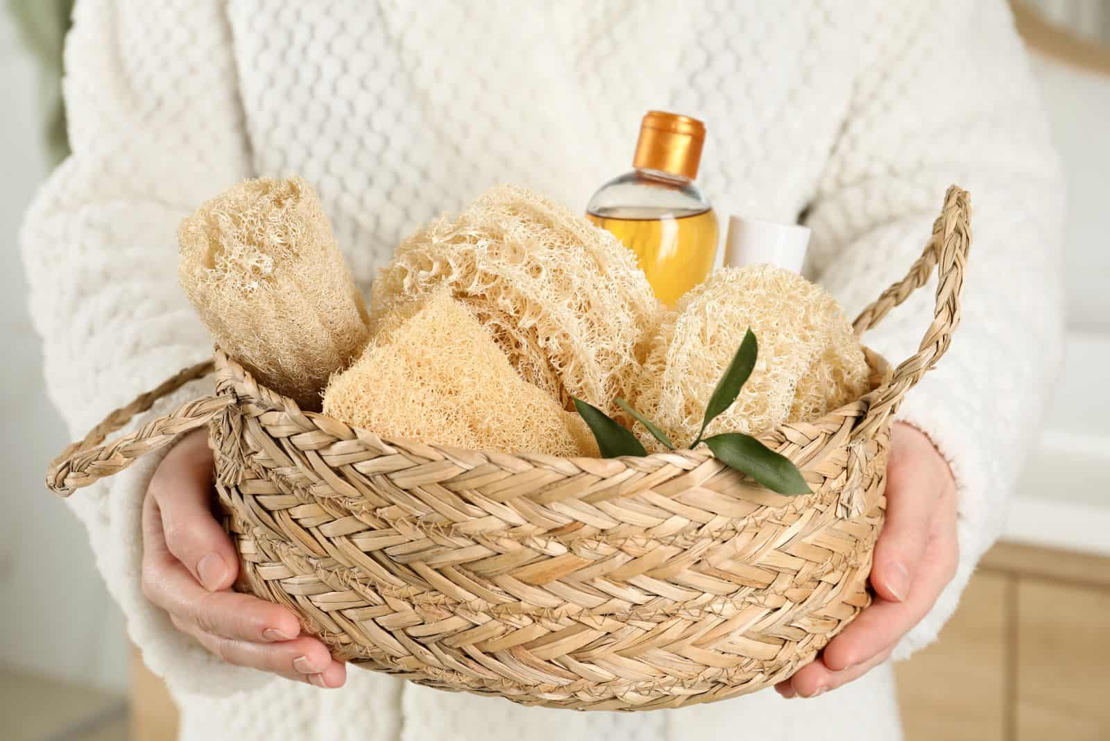 Woman holding wicker basket with natural loofah sponges in bathroom