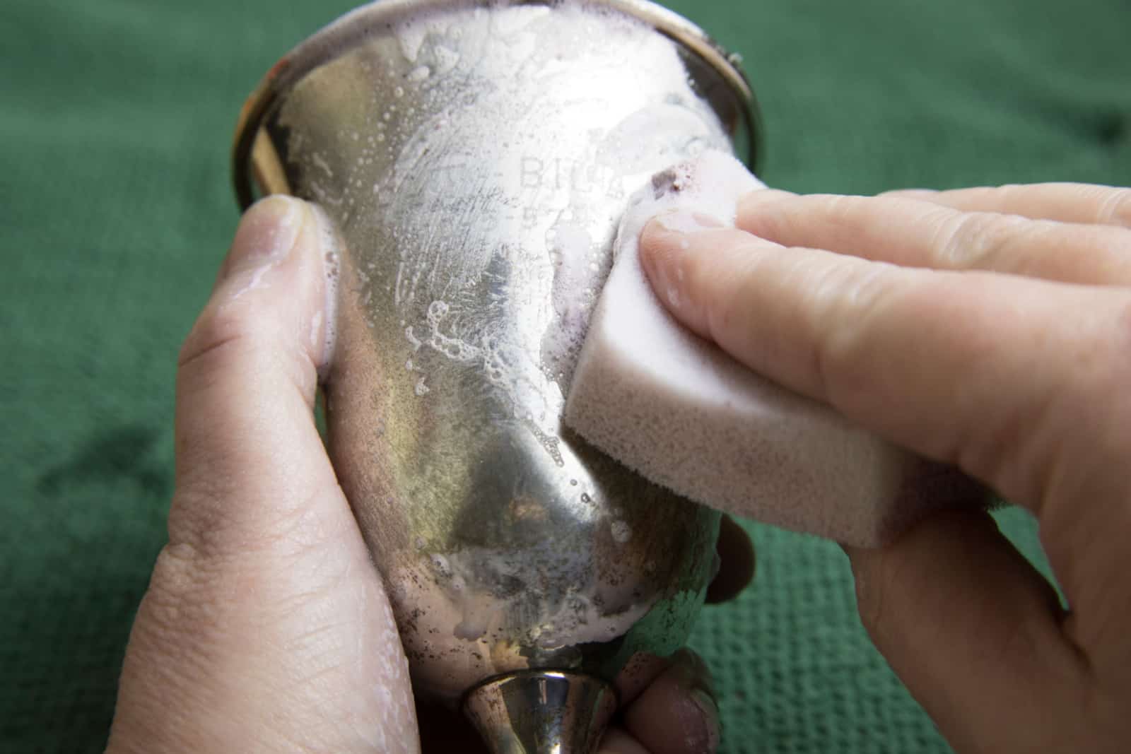 Close up of woman's hands using sponge to polish tarnish off silver goblet.