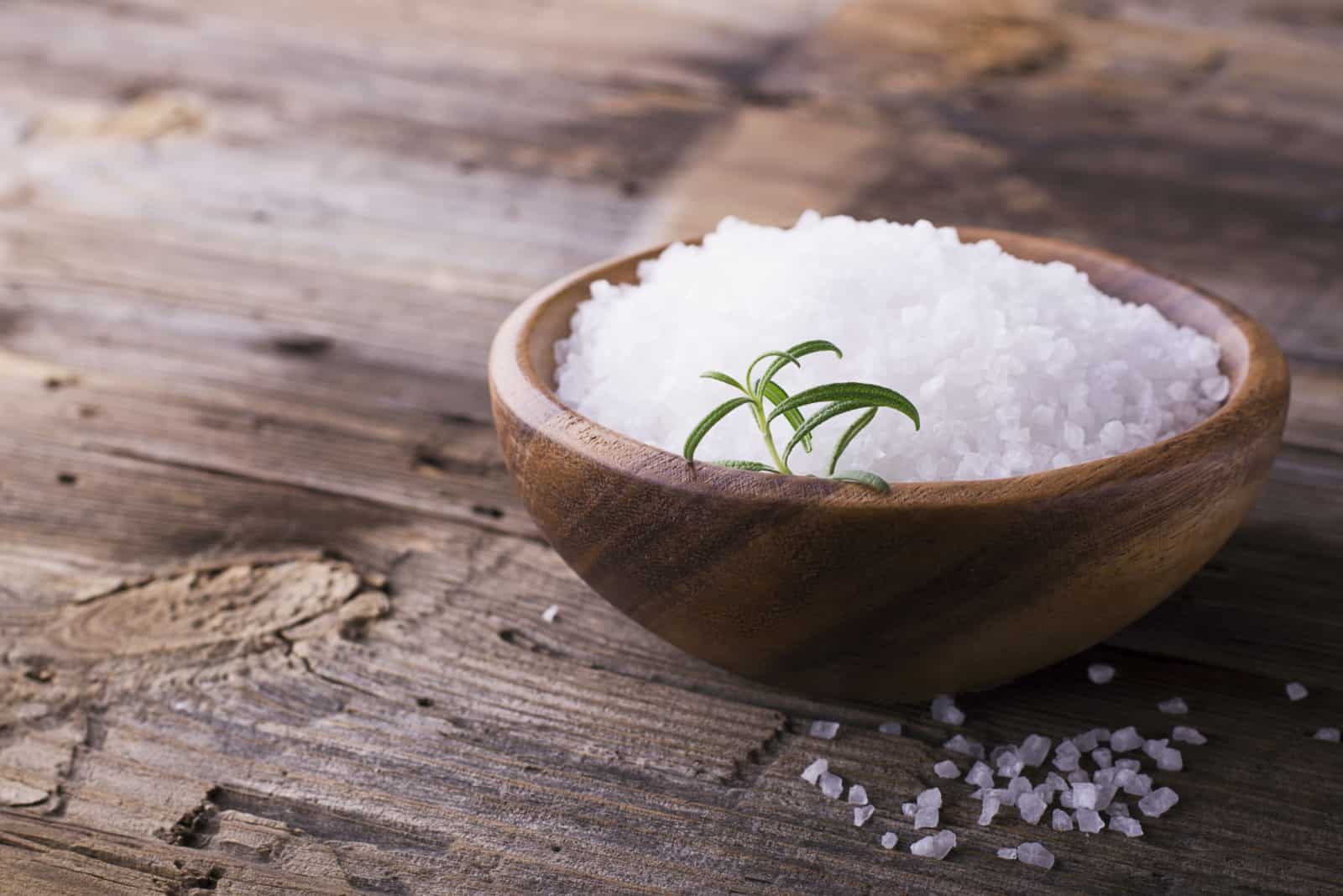 Large White sea salt in a natural wooden bowl with a sprig of fresh rosemary