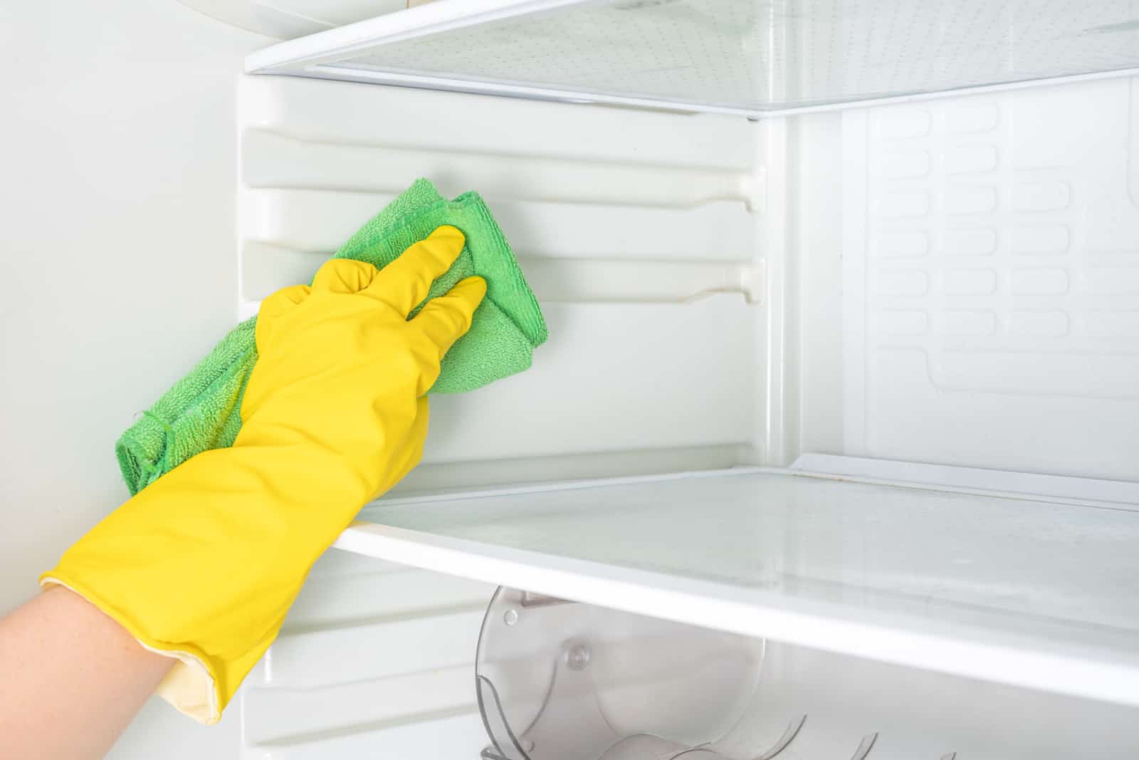Woman hand in yellow rubber protective glove cleaning white open empty refrigerator