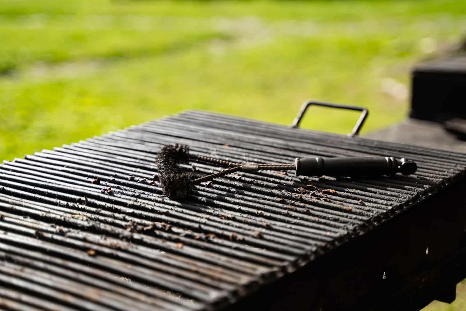 front view closeup of outdoor empty barbeque grill with black brush tool for cleaning