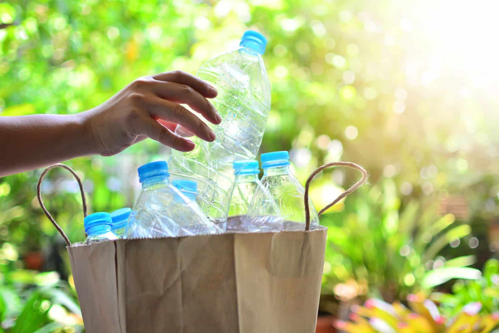 hand putting plastic bottle in paper bag 
