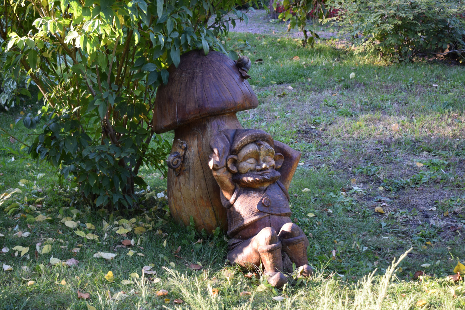 wooden sculpture of dwarf resting under a mushroom in the garden.