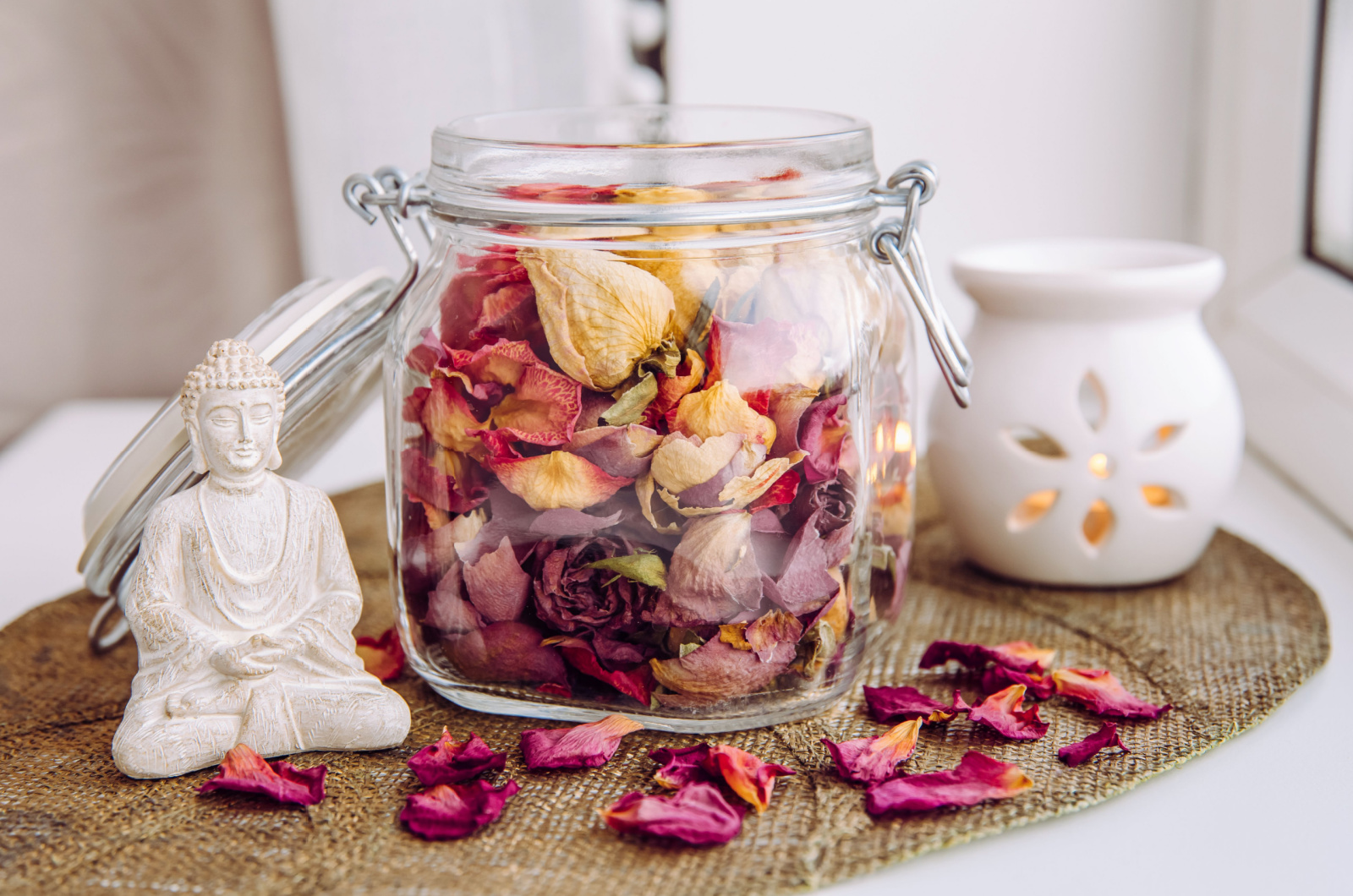 jar filled with dry rose petals, with Buddha figurine and a candle next to it