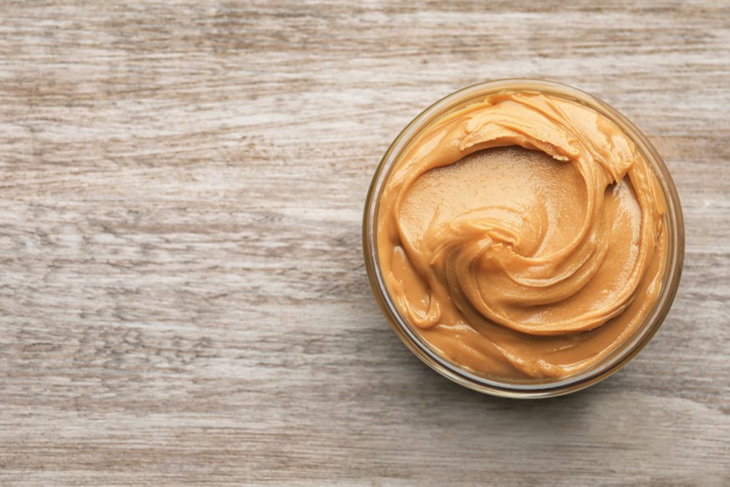Glass bowl with peanut butter on wooden background