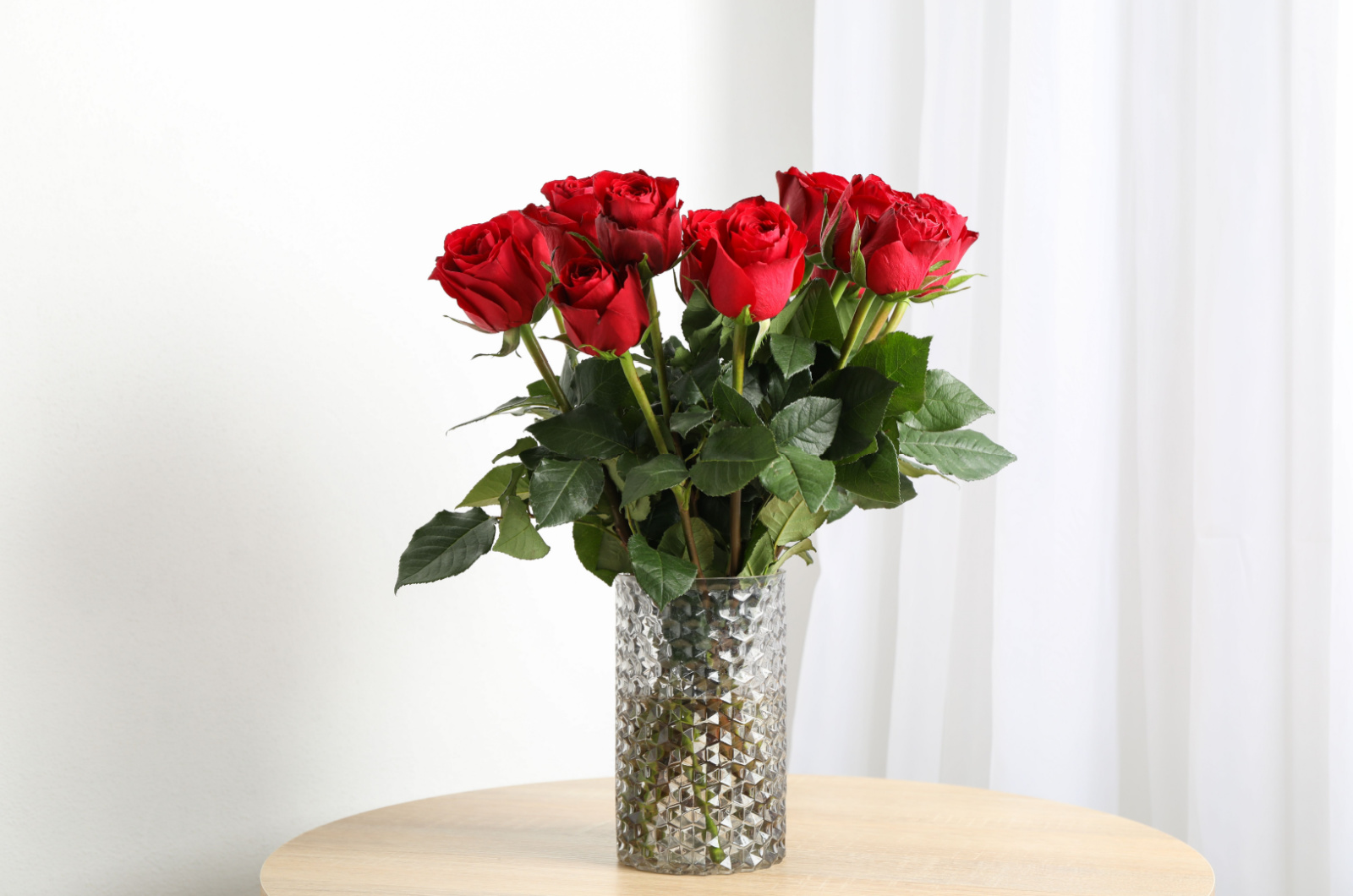 Vase with bouquet of red roses on wooden table
