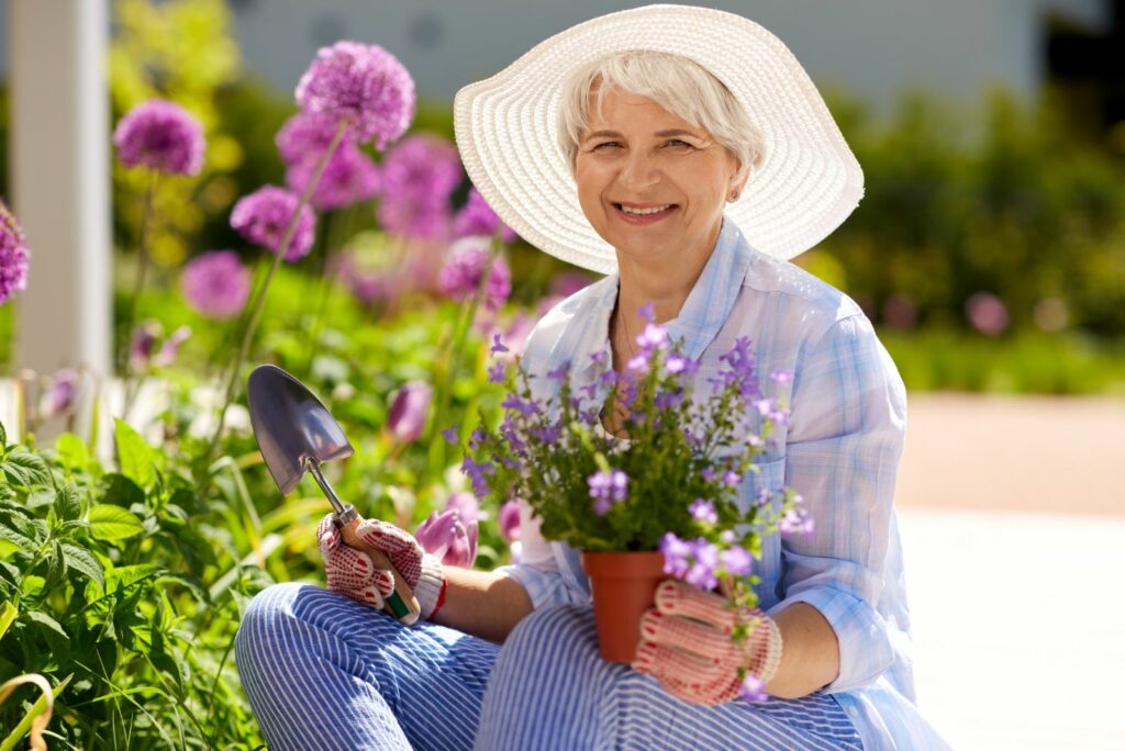 a woman with a hat holds a pot of bluebells and a transplanting tool