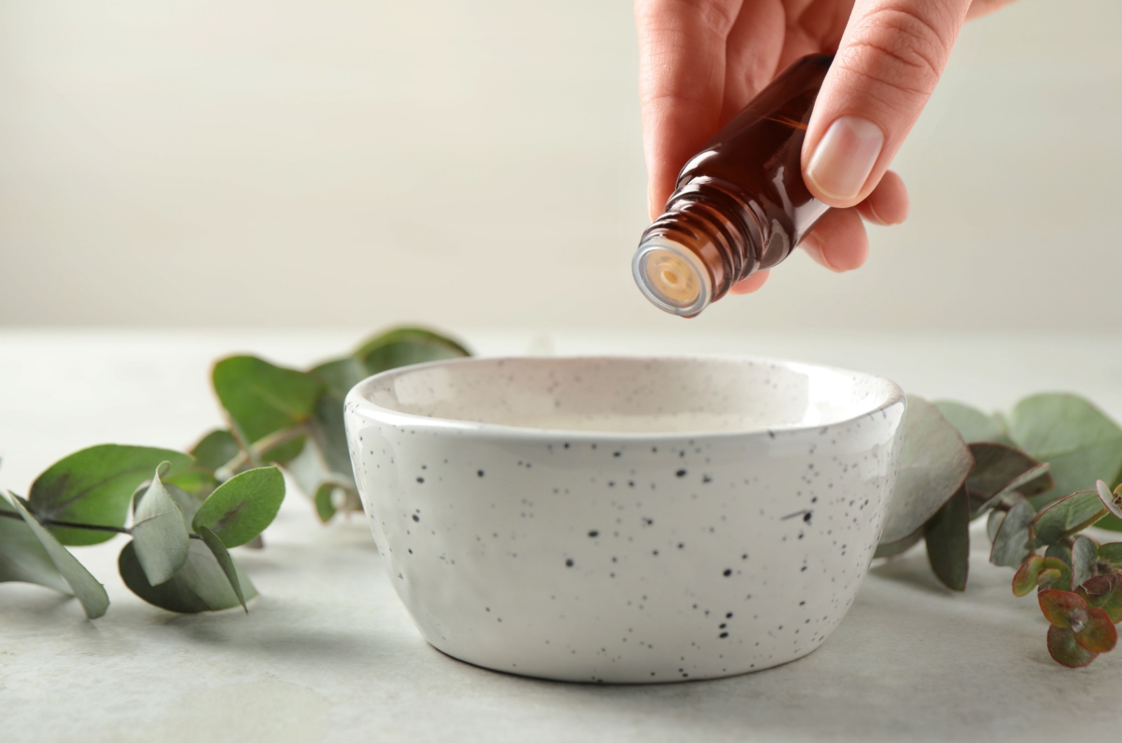 Woman dripping eucalyptus essential oil from bottle into bowl
