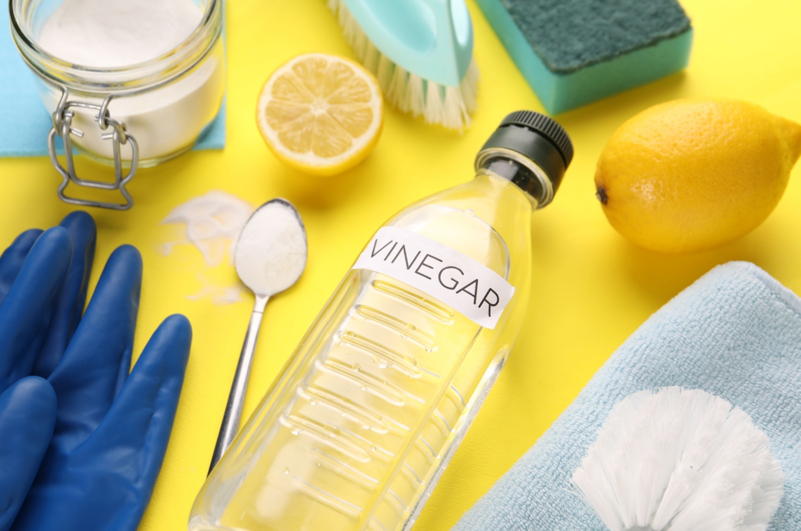 Vinegar in bottle, soda, lemons and gloves on yellow background