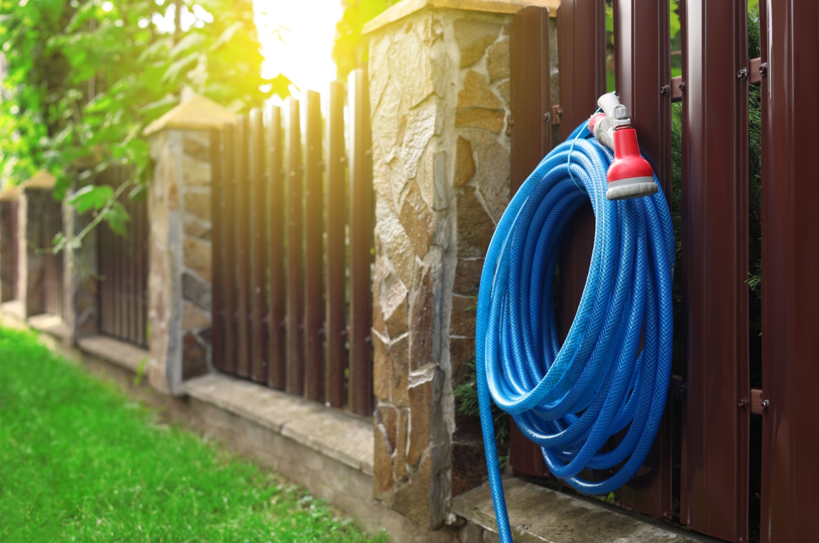 Watering hose with sprinkler hanging on wooden fence