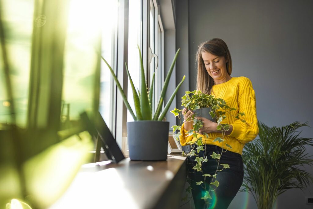 a woman stands next to the flowers and holds a pot in her hand