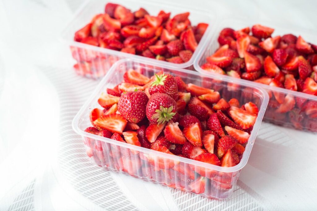 sliced pieces of strawberries in clear containers on white textile background