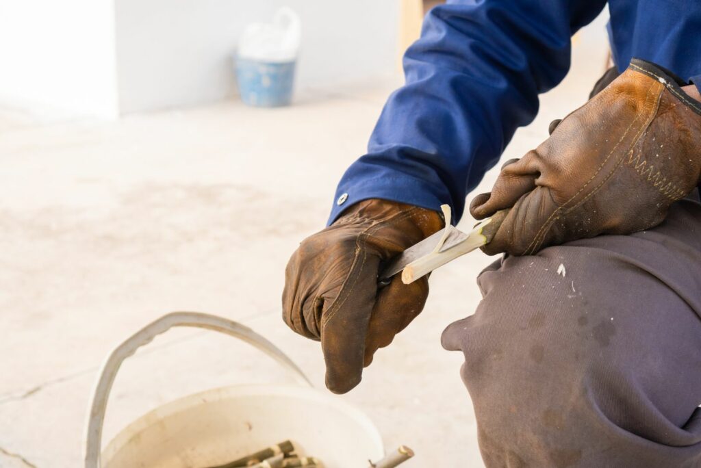 Person making a wood tree stake using a knife and protective gloves