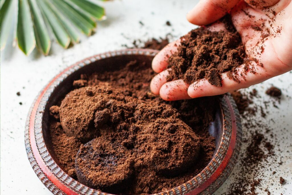 Woman's hand crumbles coffee grounds into wooden bowl