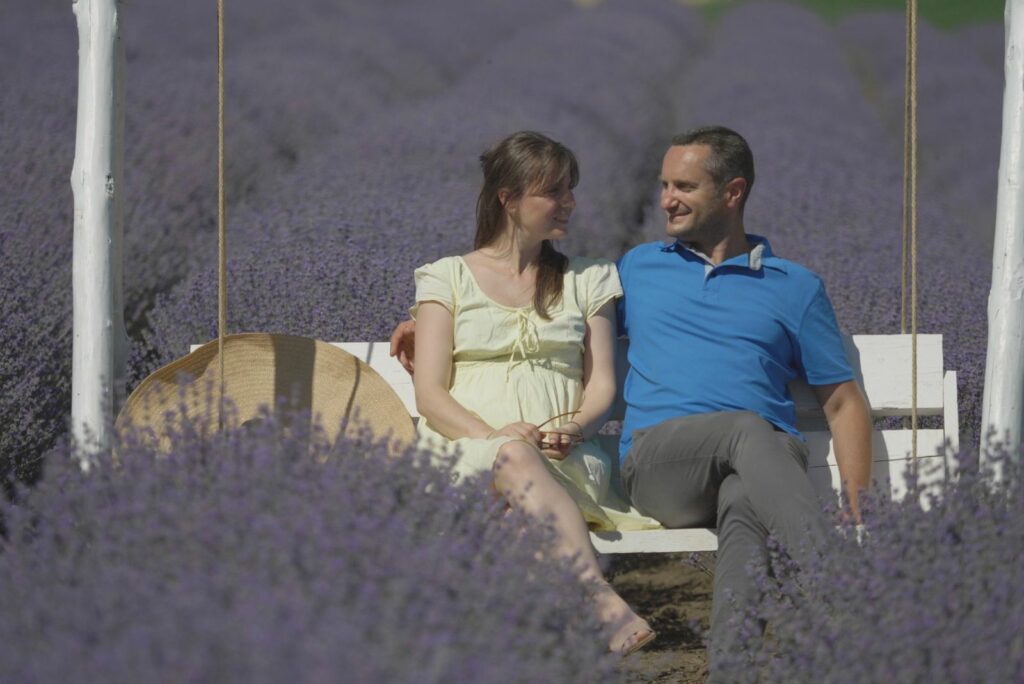 a man and a woman are sitting on a bench with lavender planted around them