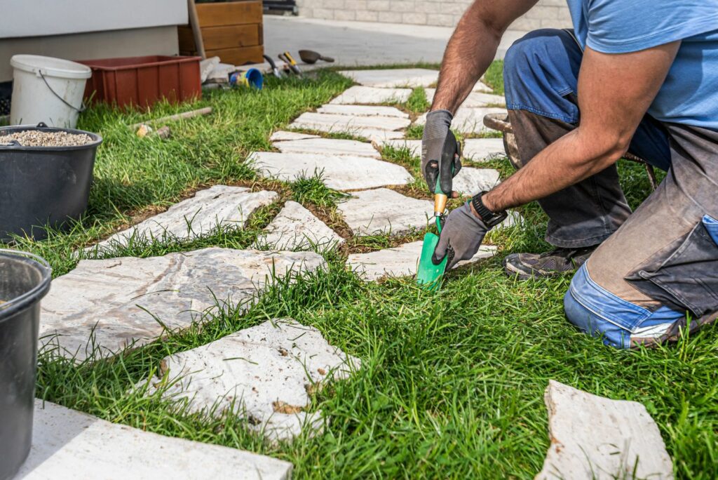 A man makes a footpath in the grass from travertine rustic stone