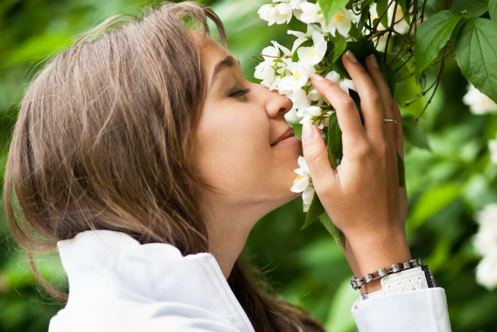 Beautiful young woman smelling white jasmin flowers