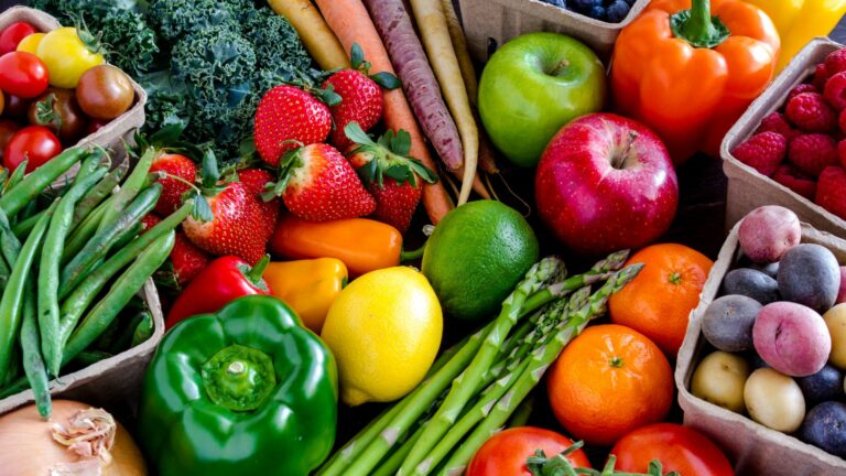 Variety of fresh raw organic fruits and vegetables in light brown containers sitting on bright blue wooden background
