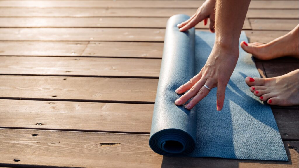 woman rolling out a yoga mat on a deck