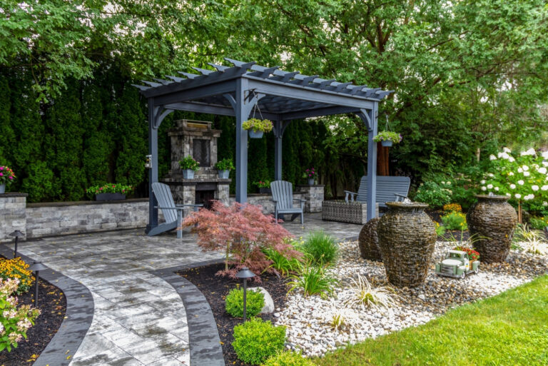 Large gray pergola on pavers with stone fireplace and waterfall urns for backyard oasis landscape design (featured image)