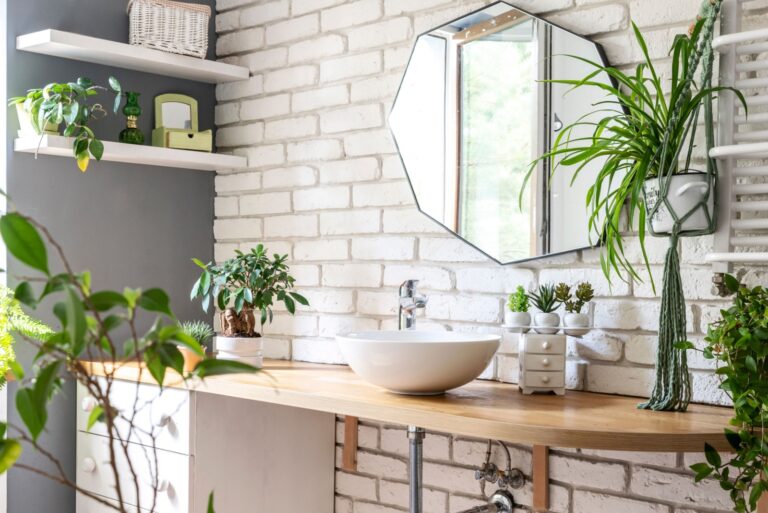 bathroom with mirror on a white bricky wall, stylish furniture, trendy wash basin and green plants