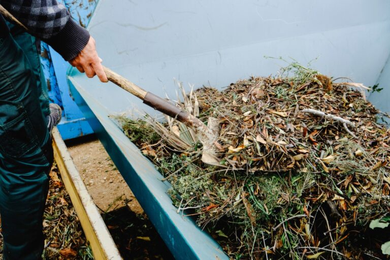 man throwing plant remains with a shovel into a large container for plant debris
