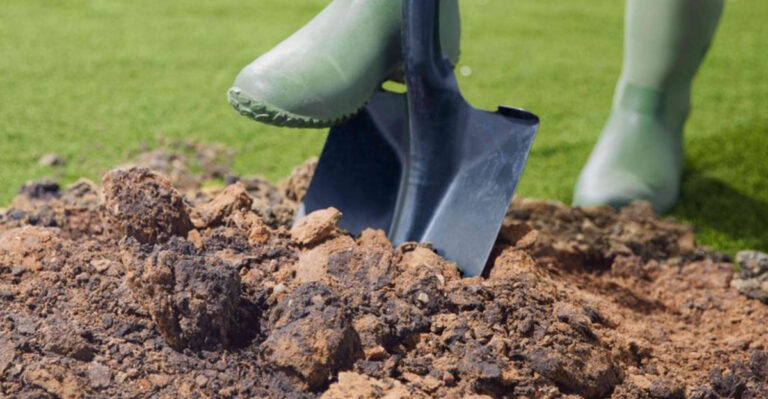 person in boots pushing shovel into soil