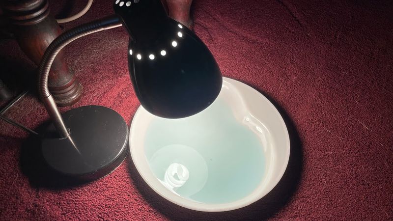 A Shallow Pan Of Soapy Water Under A Lamp